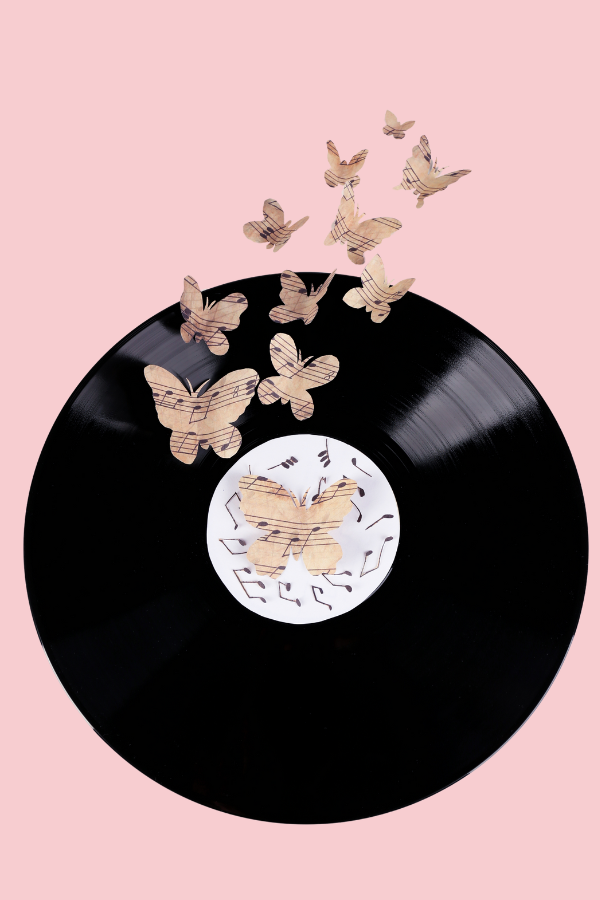 Vinyl record with paper butterflies made from sheet music. Scattered music notes. Pink Background.
