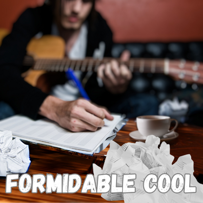 acoustic guitar across his lap. He leans over to write lyrics into a journal on a wooden table. A cup of bergamot tea in a saucer is placed to the side. Crumpled sheet music litters the table foreground.